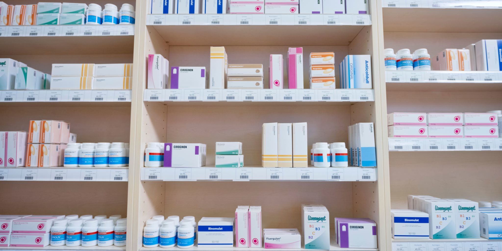 Shelves filled with various prescription medicine boxes and bottles in a pharmacy or medical supply room, organised and labelled.