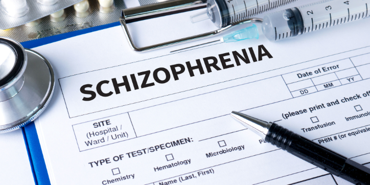 A medical form labelled Schizophrenia is surrounded by a stethoscope, syringe, pills, and a pen, suggesting a clinical context related to mental health diagnosis or treatment.