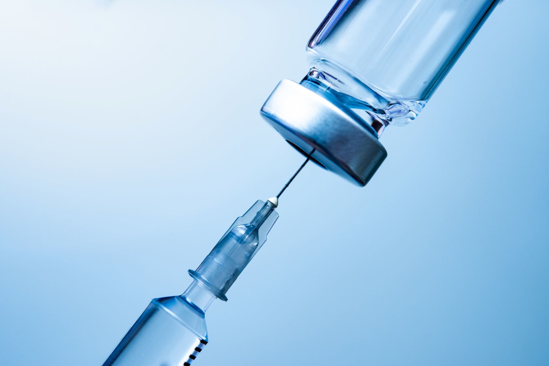 A close-up of a syringe needle being inserted into a vial, set against a blue background, symbolising vaccination or medical injection.
