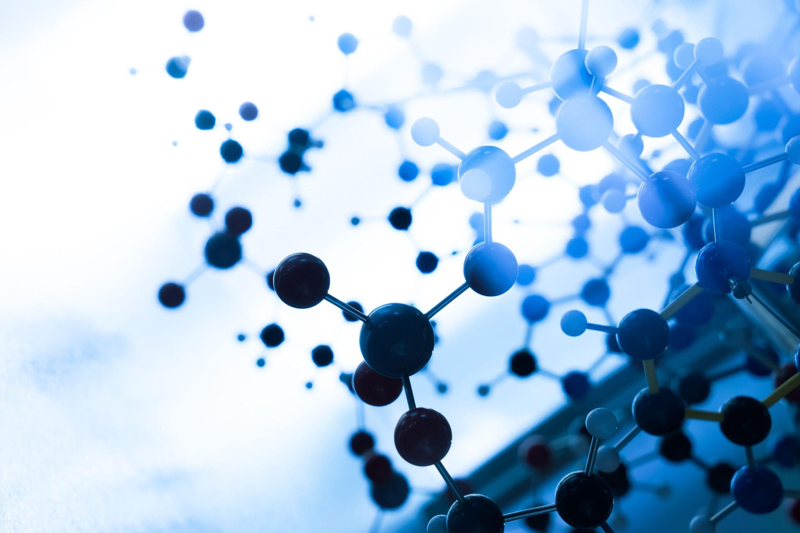 A close-up view of a molecular model with interconnected atoms depicted as coloured spheres and sticks, set against a blurred blue and white background.