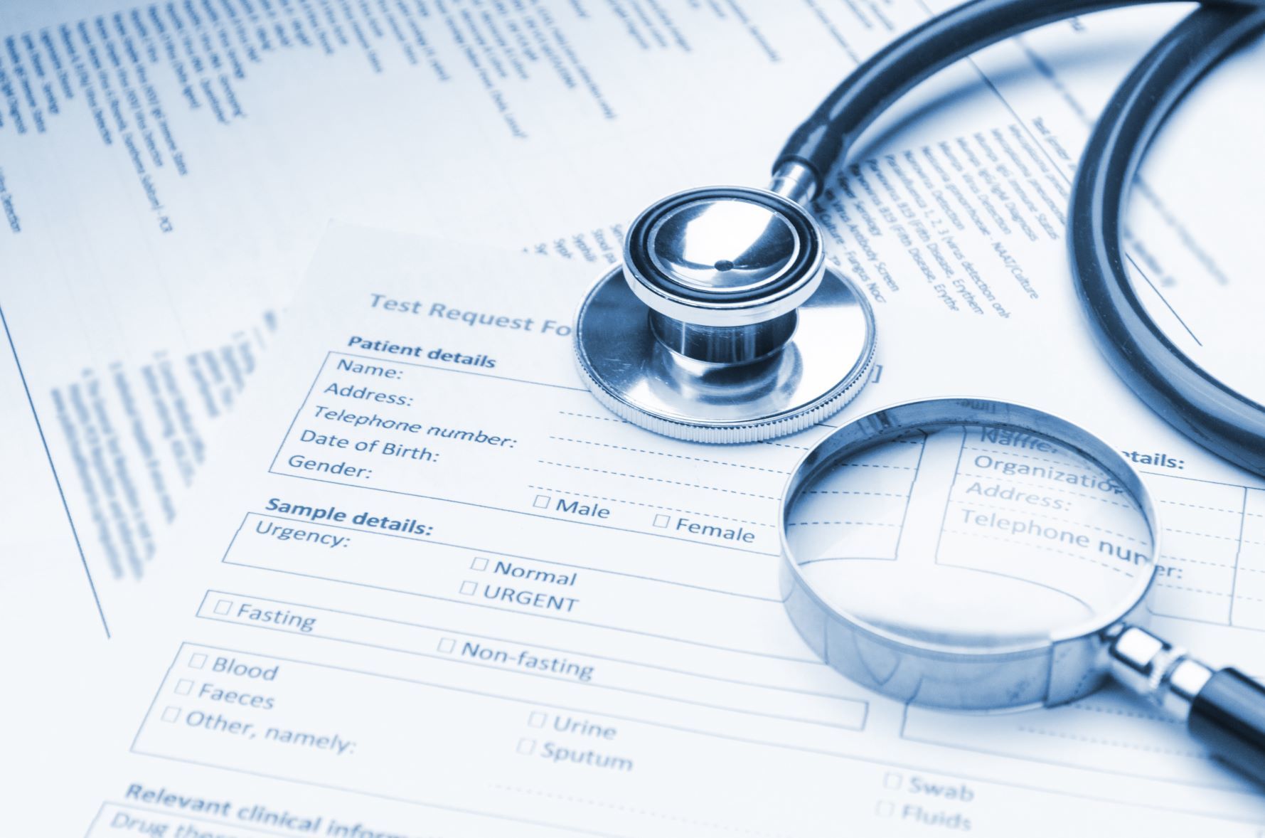 A stethoscope and magnifying glass rest on top of a medical test request form, with blank fields for patient information and test details.