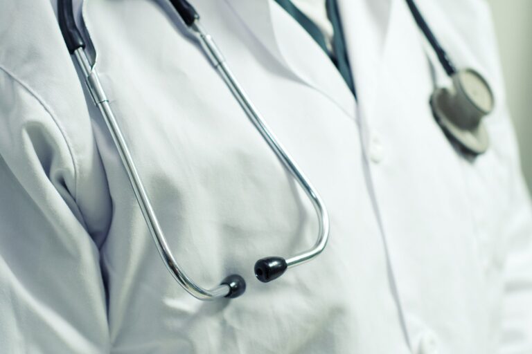 A close-up of a person wearing a white lab coat with a stethoscope draped around their neck, suggesting a healthcare professional.