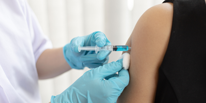A healthcare professional wearing blue gloves administers an injection into a person's upper arm whilst holding a cotton wool ball on the skin.