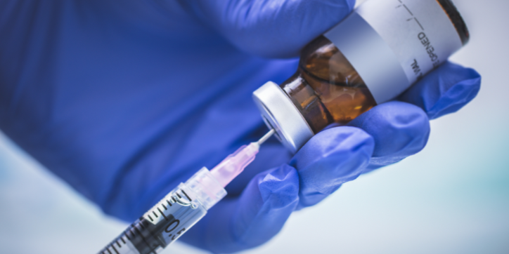 A gloved hand holds a vial whilst drawing liquid with a syringe.